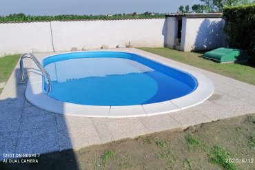 Piscina interrata ovale con rivestimento azzurro, scala in inox e bordo bianco antiscivolo.