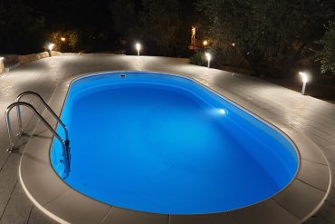 Piscina ovale interrata Skyblue 600 con comodi scalini in pietra, corrimano inox e lampioni in stile rustico, per un ingresso elegante e sicuro in acqua.