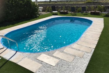 Piscina interrata Skyblue 700×350×120 cm con bordo in lastre di pietra e ghiaia bianca, completa di lettini relax su prato verde per momenti di puro benessere.