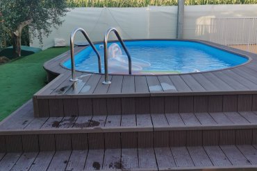 Piscina seminterrata Skyblue in lamiera d’acciaio con liner azzurro, circondata da un elegante deck WPC effetto legno e prato sintetico antiscivolo, per un progetto outdoor moderno e a bassa manutenzione.