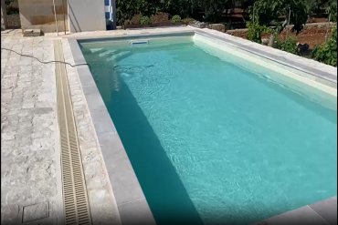 piscina rettangolare interrata in pannelli d’acciaio Futura Classica 7,8×3 m: bordo in pietra, rivestimento liscio e sistema di skimmer a sfioro.